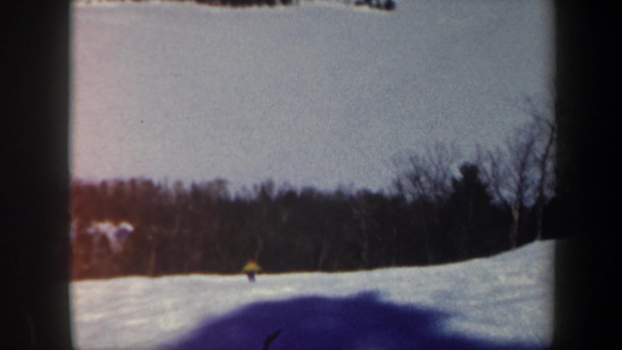 1962 Vermont 8mm frame showing a small lone skier on a snow-covered slope with winter woods and soft film edges.