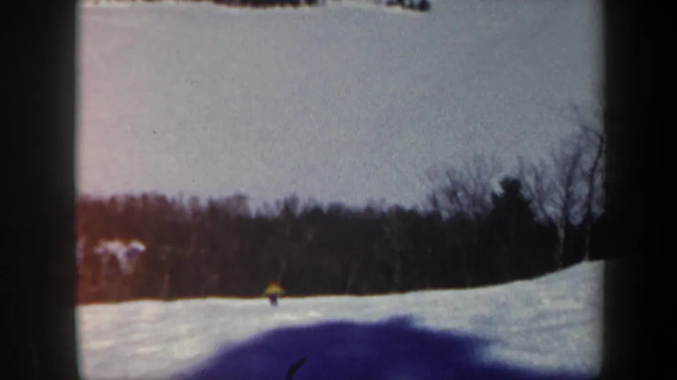 1962 Vermont 8mm frame showing a small lone skier on a snow-covered slope with winter woods and soft film edges.