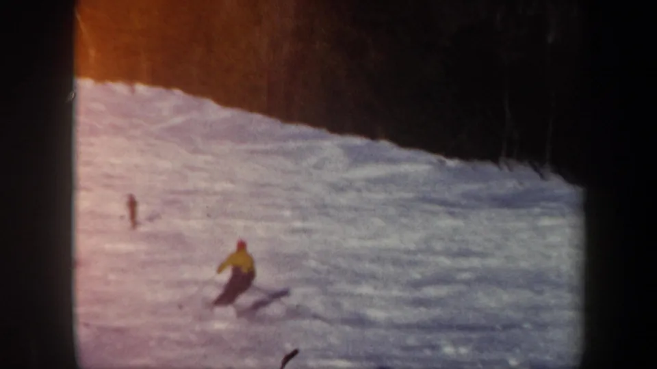 1962 Vermont 8mm frame showing the skier turning on the open snow, with warm color shift and wooded background visible.