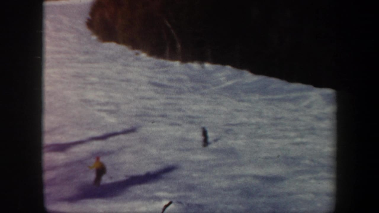 1962 Vermont 8mm frame showing two distant skiers descending a snowy mountain slope under long shadows.
