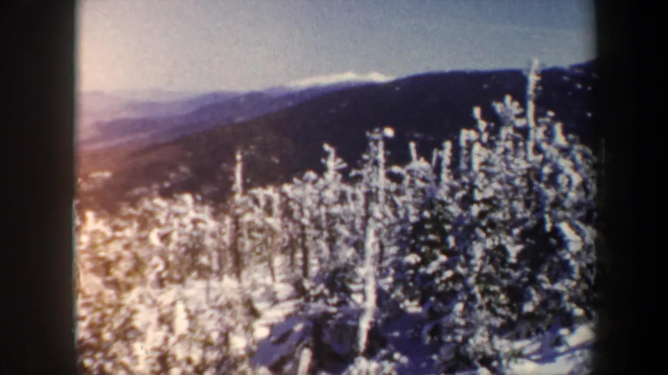 1962 Vermont 8mm frame with sunlit snow-covered trees in front of dark mountain ridges.