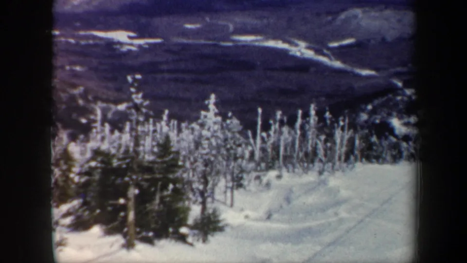 1962 Vermont 8mm frame with frosted trees, snowbanks, and distant wooded mountains in soft color film grain.