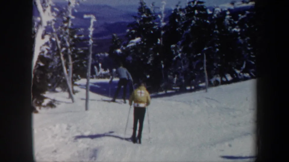 1962 Vermont home-movie frame of a skier descending or traversing a snowy slope with forested mountain scenery behind.