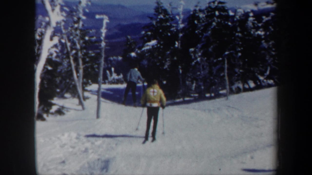 1962 Vermont 8mm frame showing two skiers on a snowy slope between trees, with the nearer skier in a yellow jacket.