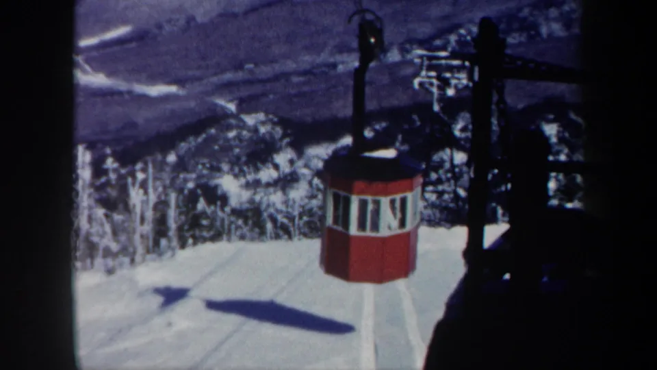 1962 Vermont 8mm frame showing a red octagonal gondola on a snowy mountain cableway above trees and a distant valley.