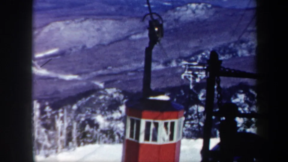 1962 Vermont 8mm frame with the red gondola below overhead cable hardware, snowy evergreens, and valley landscape.