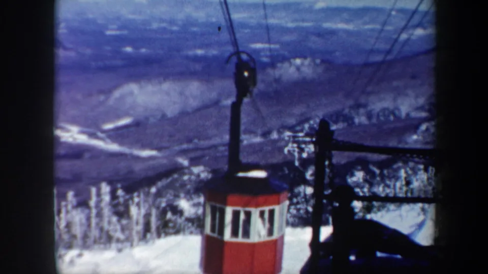 1962 Vermont home-movie frame showing the red gondola on its mountain cableway with snow, evergreens, and valley beyond.