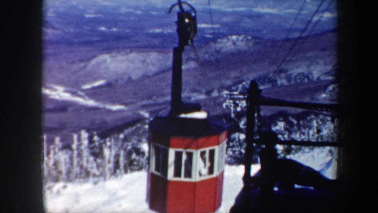 Red gondola cabin and cable structure against snowy ridges and blue sky.