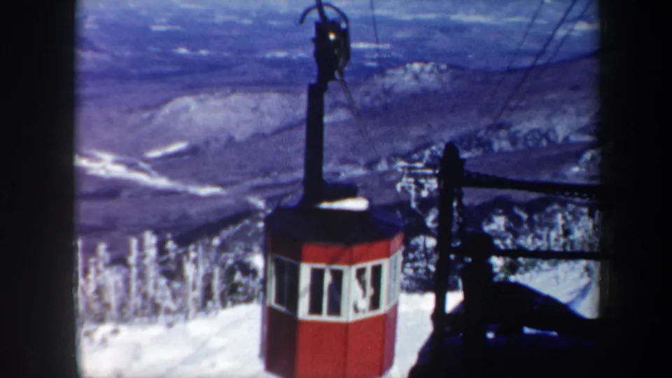 1962 Vermont 8mm frame with a red gondola cabin moving along cables above a winter mountain panorama.