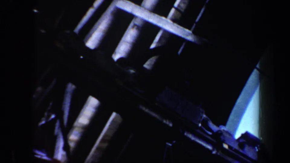 1962 Vermont home-movie frame showing the gondola lift's mechanical structure in shadow with snow-covered mountain terrain in the background.
