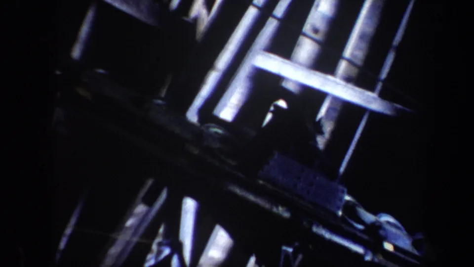 1962 Vermont 8mm frame focused on the lift tower mechanism and cable hardware, with winter slopes visible behind the structure.