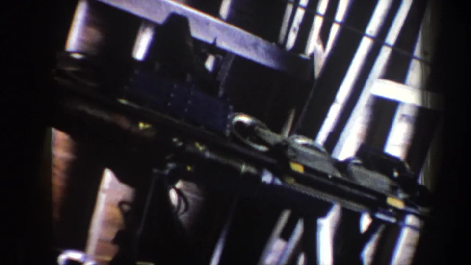 Final close frame of Vermont ski lift machinery, showing rods, wheels, brackets, and heavy shadows in vintage 8mm color.