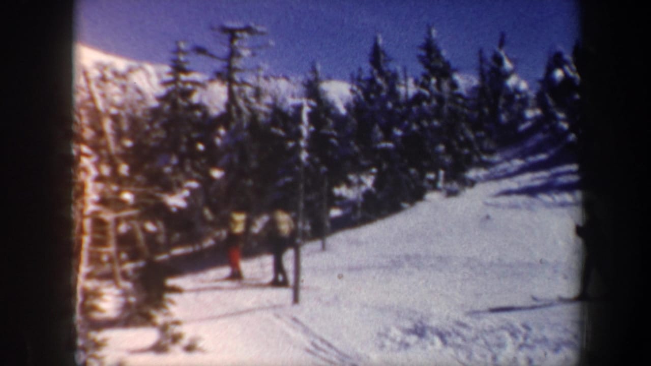 1962 Vermont home-movie frame with skiers waiting near a lift-area pole on a snowy mountain slope.