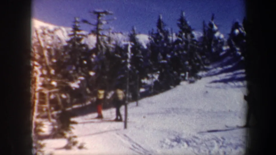 1962 Vermont home-movie frame with skiers waiting near a lift-area pole on a snowy mountain slope.
