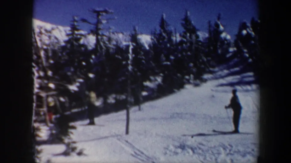 1962 Vermont 8mm frame showing a lone skier standing on a snow-covered slope with evergreens behind.