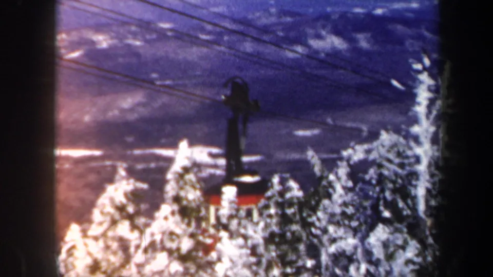 1962 Vermont 8mm frame with the tram cabin nearly hidden by snow-covered evergreens and color-shifted winter terrain beyond.
