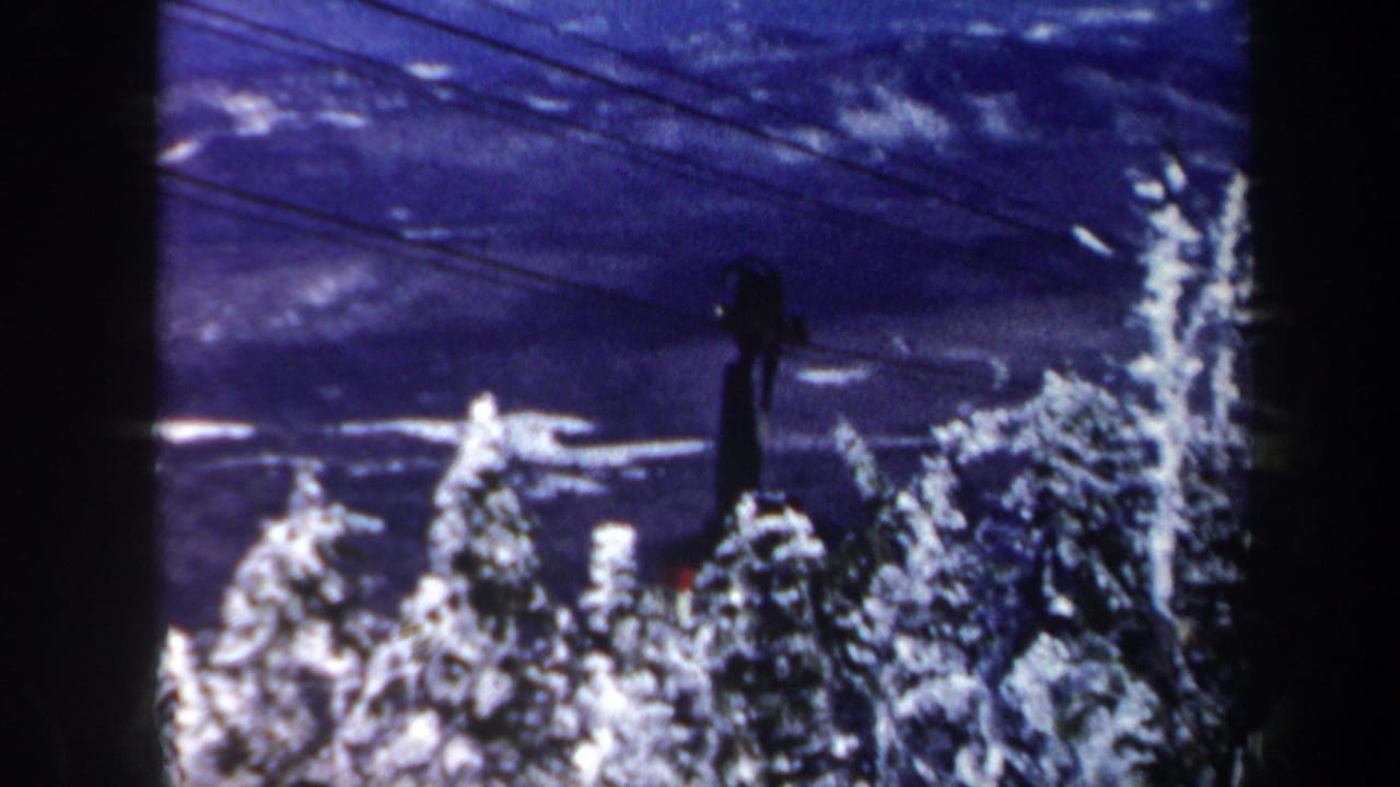 1962 Vermont home-movie frame showing a dark cable car above snow-covered evergreens with a blue-purple winter cast.