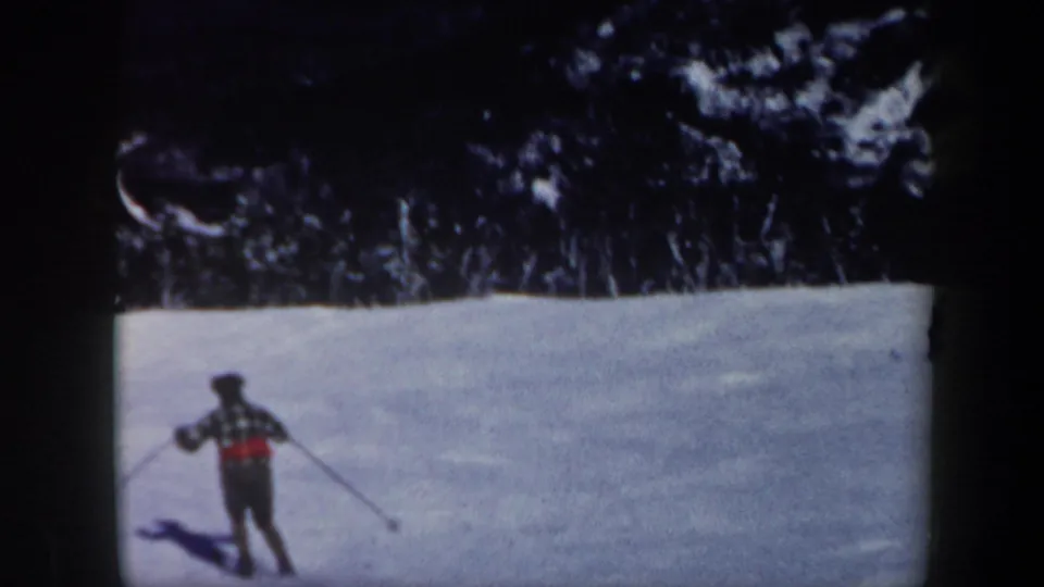A distant skier in winter clothing crosses a snowy Vermont slope, framed by dark trees and aged 8mm borders.