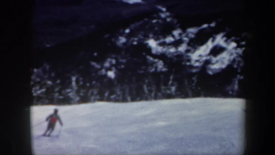 Distant skier descends a broad snowy Vermont ski slope, with dark evergreen trees and soft 8mm grain visible.