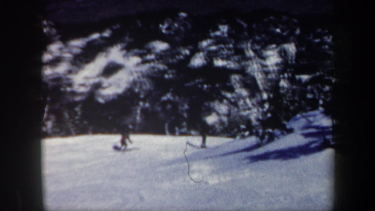 1962 Vermont 8mm frame showing a distant skier crossing a snow-covered slope beside a wooded forest edge.