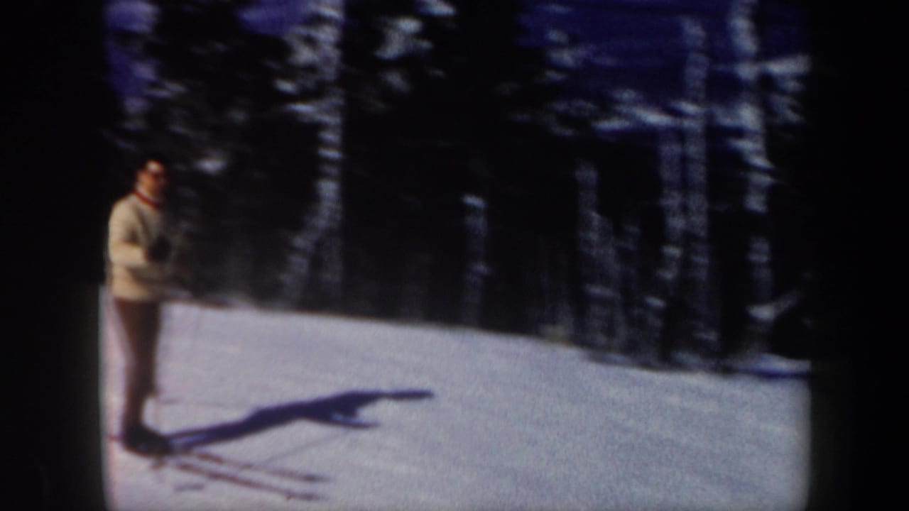 1962 Vermont home-movie frame of an adult male skier standing on a snowy hillside with poles and long shadows.