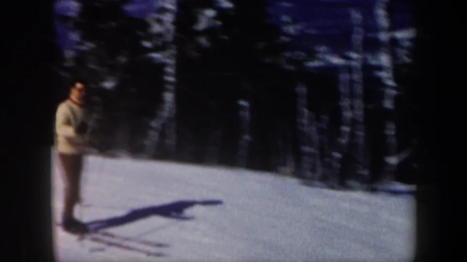 1962 Vermont home-movie frame of an adult male skier standing on a snowy hillside with poles and long shadows.