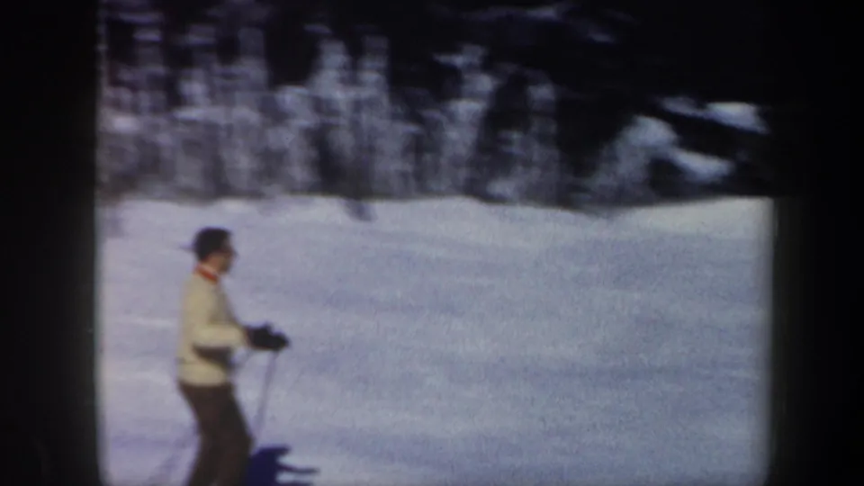 Adult skier seen in profile on a blue-tinted snowy slope, blurred by handheld 8mm motion in Vermont footage from 1962.