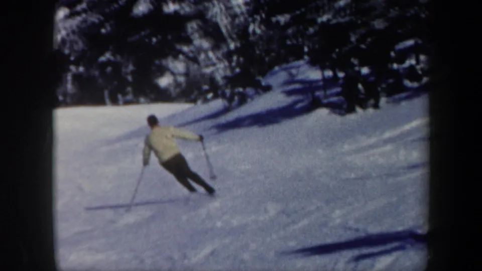 1962 Vermont frame showing an adult skier leaning into a downhill turn across a bright wooded snow slope.