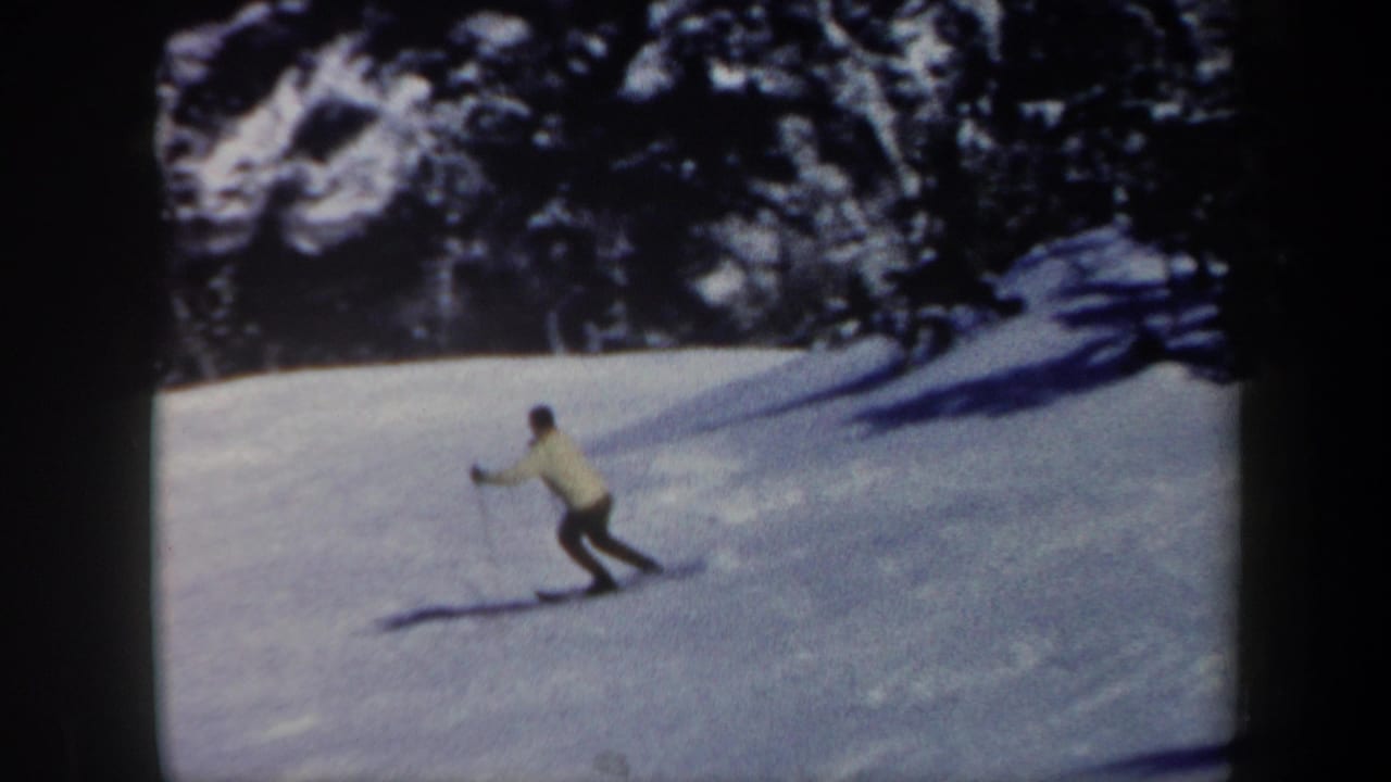 Skier in a light jacket turns across a snowy slope with evergreen trees behind.