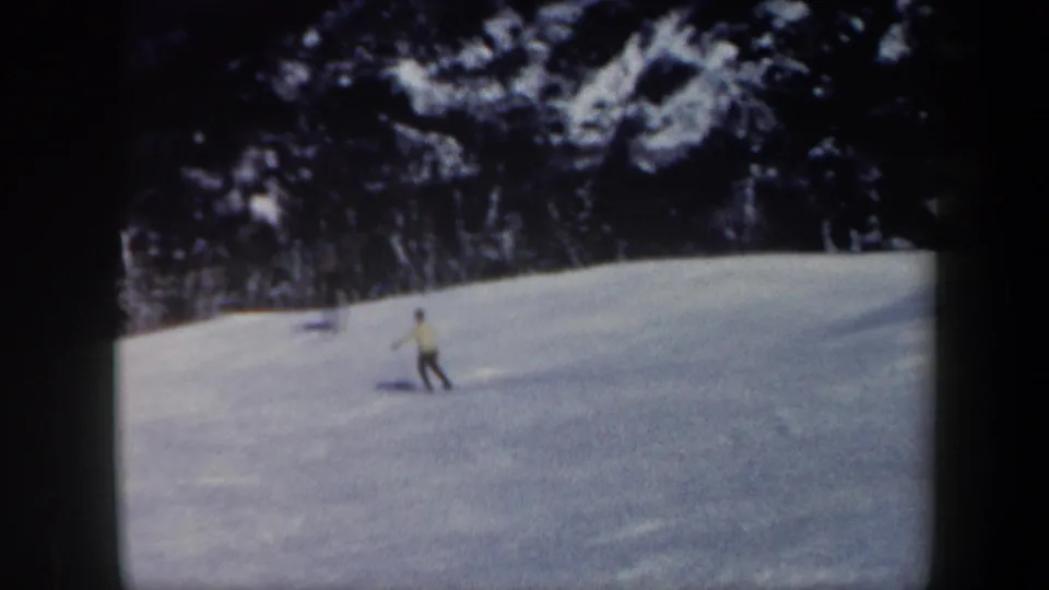 A small figure on skis crosses the lower snowfield in the 1962 Vermont scene, framed by soft-focus 8mm edges and evergreen woods.