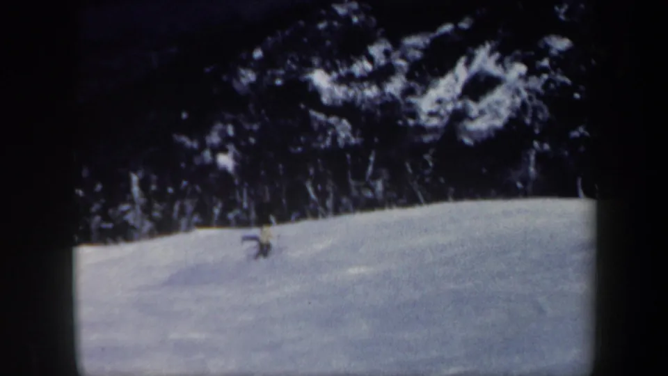 Near the end of the clip, the skier is small and low on the Vermont slope, with dark evergreens and blue-toned snow visible in the 8mm frame.