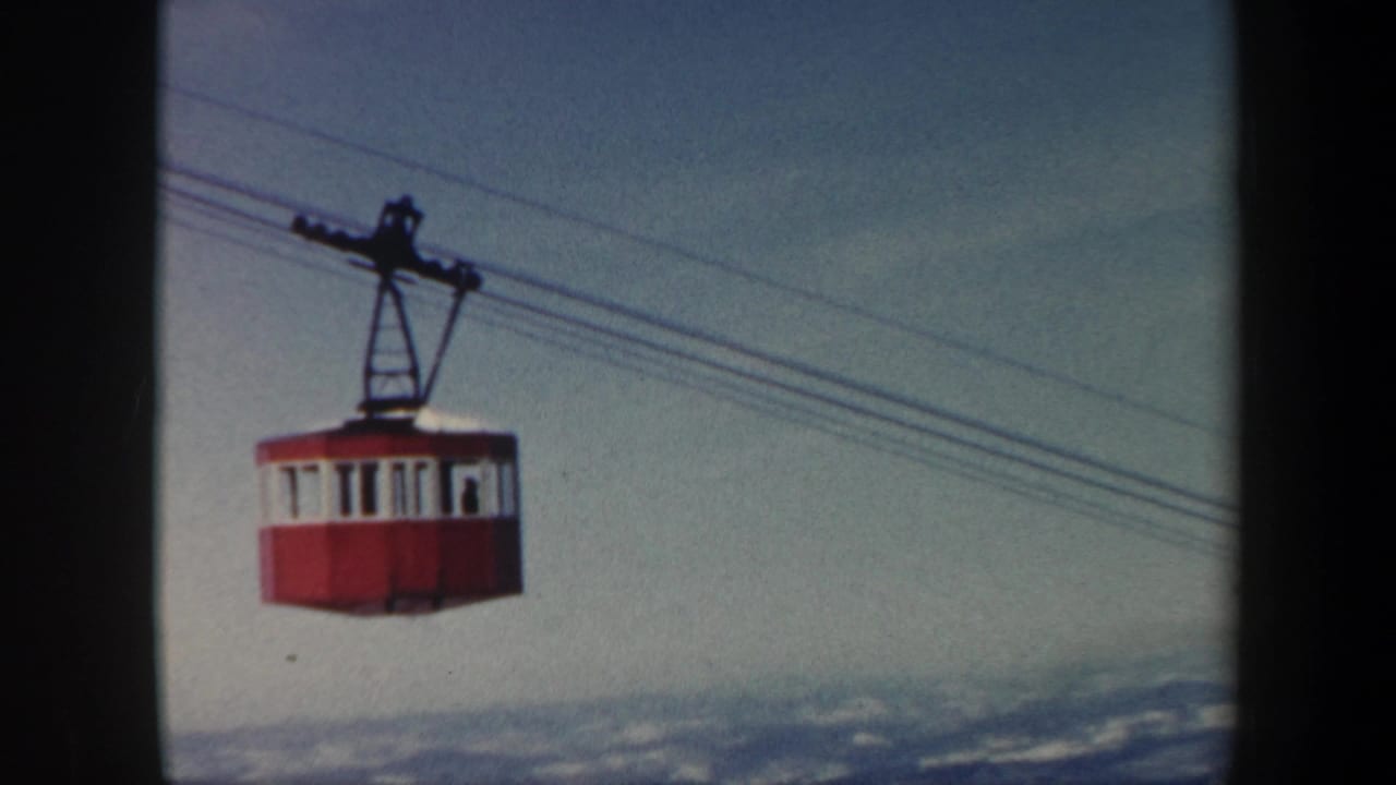 Cable car moving along wires with snowy mountains visible below.
