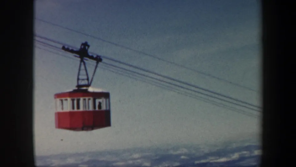 Red and white aerial tram cabin over a snow-dusted Vermont mountain landscape in a 1962 home-movie frame.