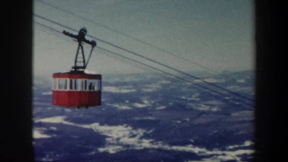 Red and white Vermont cable car suspended high above a broad snow-dusted mountain landscape, filmed on 8mm in 1962.