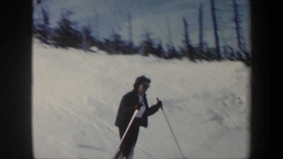 A helmeted skier in dark winter clothing appears on a snowy Vermont slope, holding ski poles against a pale snowbank.