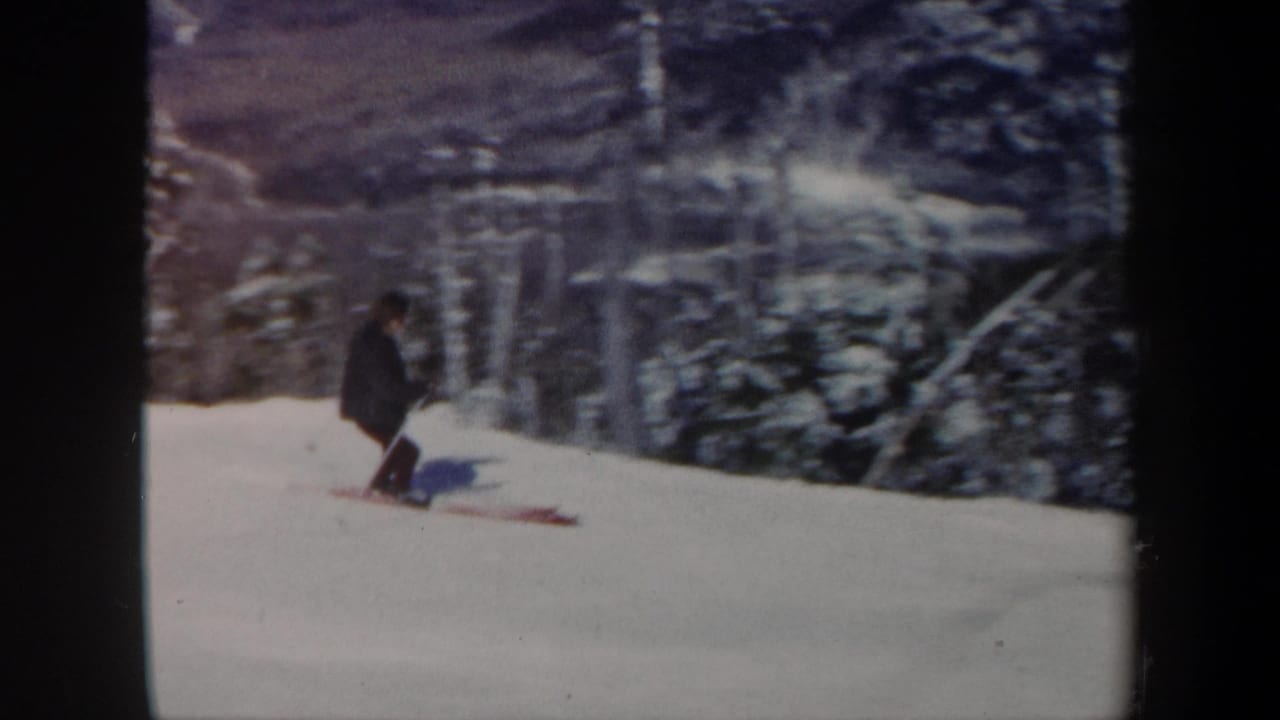 1962 Vermont 8mm frame showing a skier in dark winter clothing moving across a snowy wooded slope.
