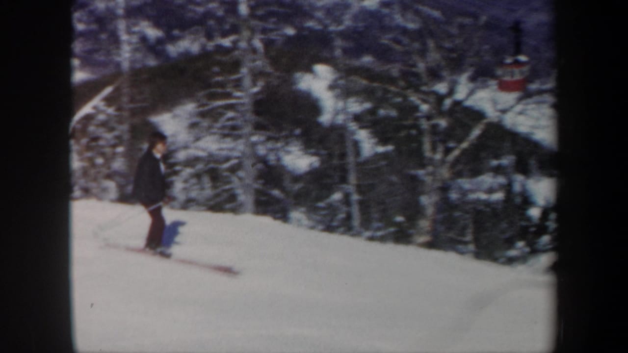 1962 Vermont home-movie frame of a skier passing a wooded section of snow-covered slope.