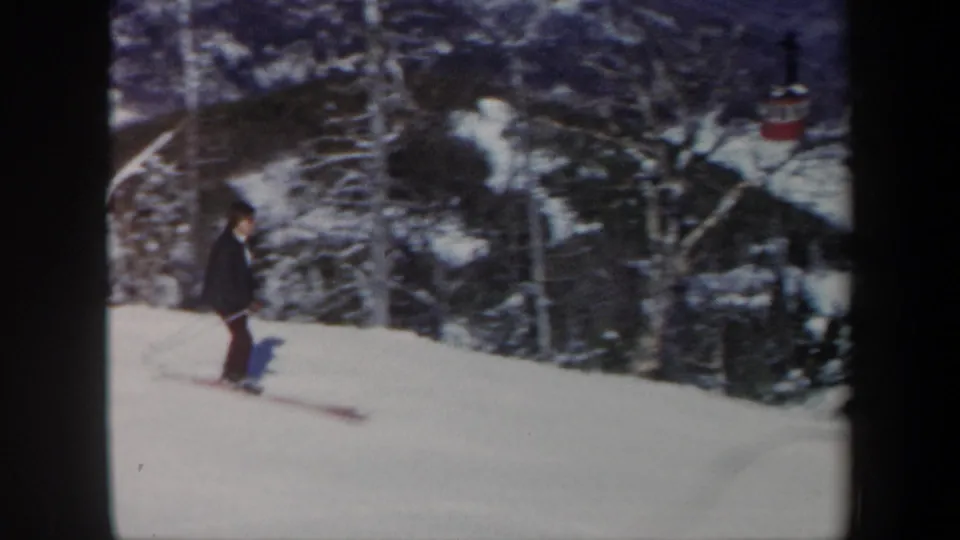 1962 Vermont home-movie frame of a skier passing a wooded section of snow-covered slope.