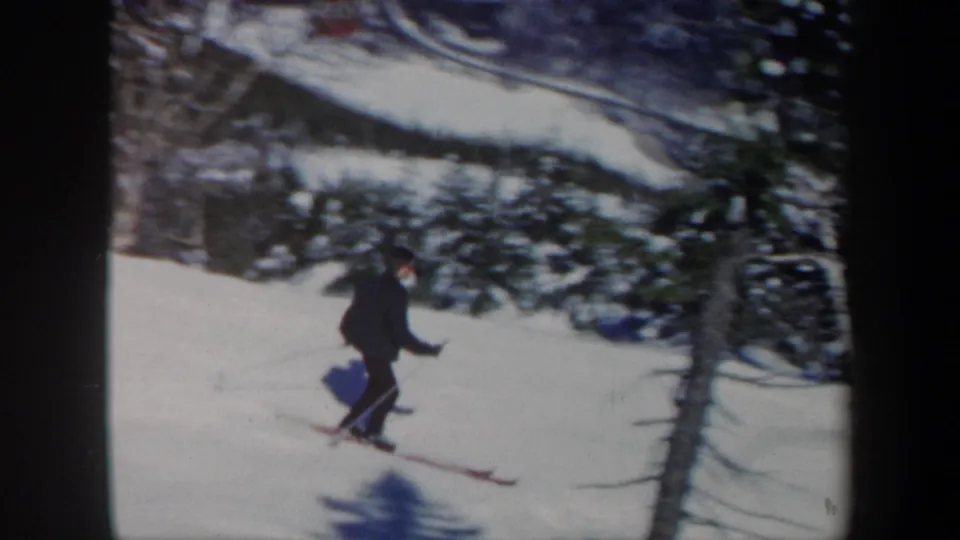 1962 Vermont 8mm frame showing the skier moving past a foreground tree on a bright snowy slope.