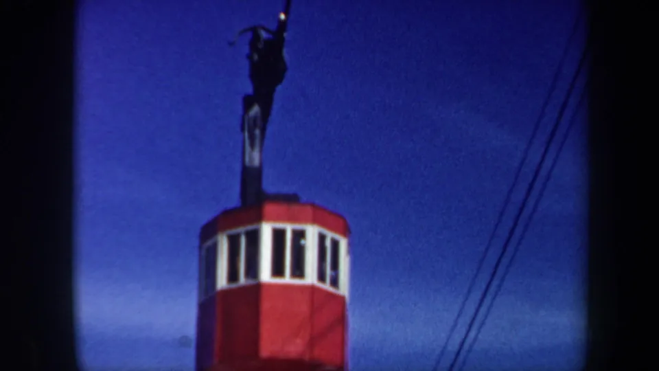 1962 Vermont 8mm still of a red cable-car cabin with white-trimmed windows ascending on cables under a deep blue sky.