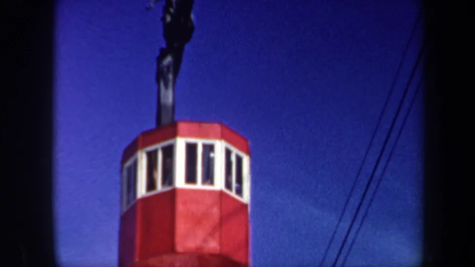 1962 Vermont home-movie frame showing the cable car continuing upward, its red cabin and white windows set below dark cables.