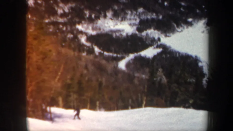 1962 Vermont frame showing the skier near the base of a snowy run, with wooded hills behind and warm 8mm color flare at the side.