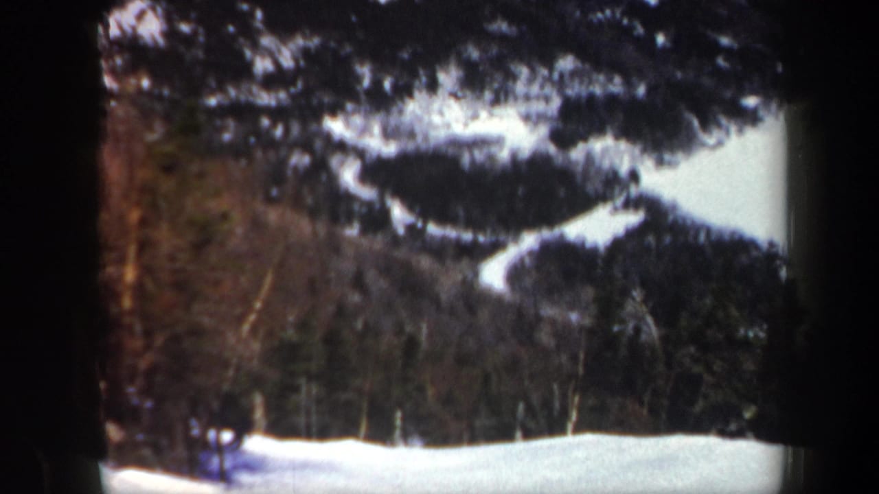 1962 Vermont home-movie frame showing snowy mountain trails, winter trees, and a small distant figure near the lower left.