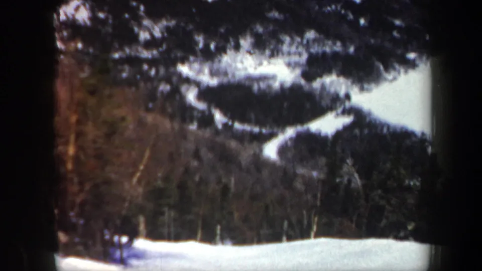 1962 Vermont home-movie frame showing snowy mountain trails, winter trees, and a small distant figure near the lower left.