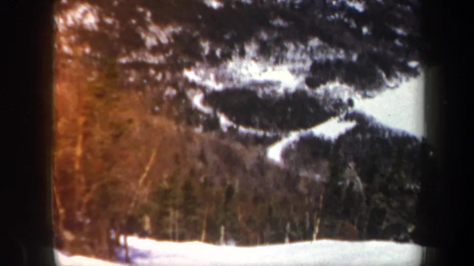 1962 Vermont 8mm frame showing a snowy mountain slope, winding trails, dark forest, and pronounced home-movie border artifacts.