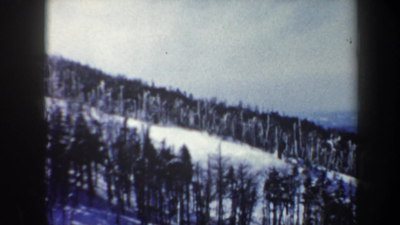 1962 Vermont 8mm frame of a snow-covered mountain slope with winter trees and hazy distance beyond the ridge.