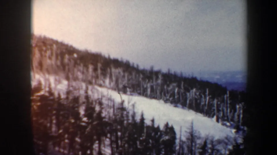 1962 Vermont 8mm frame showing a broad snowy hillside through winter forest with a muted valley view in the distance.