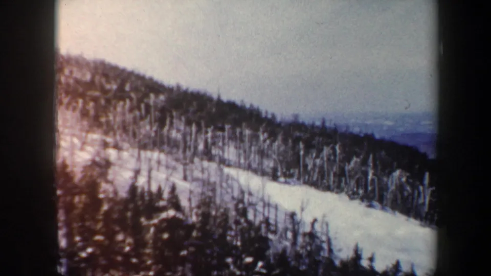 1962 Vermont 8mm frame of a snowy hillside framed by winter trees, with soft color fading and distant landscape haze.