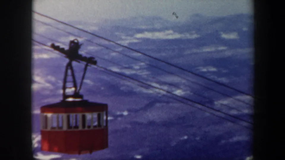 1962 Vermont 8mm frame showing a red gondola cabin suspended on cables over snowy mountain ridges.