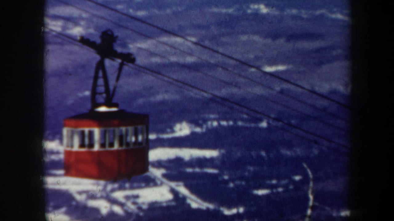 Red cable car hanging from overhead lines against a distant mountain backdrop.